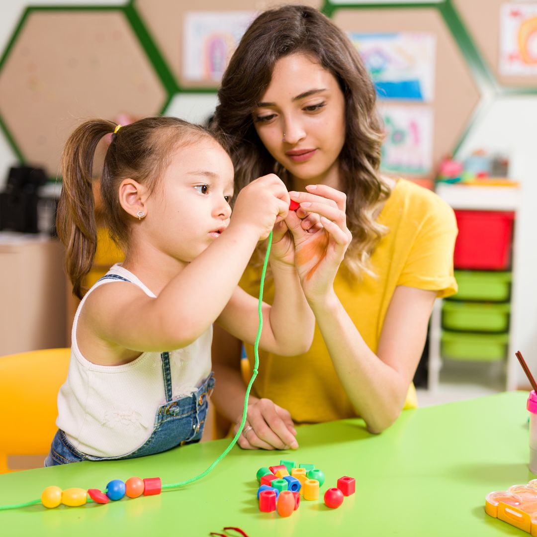 Preschool teacher helping student put beads on a string