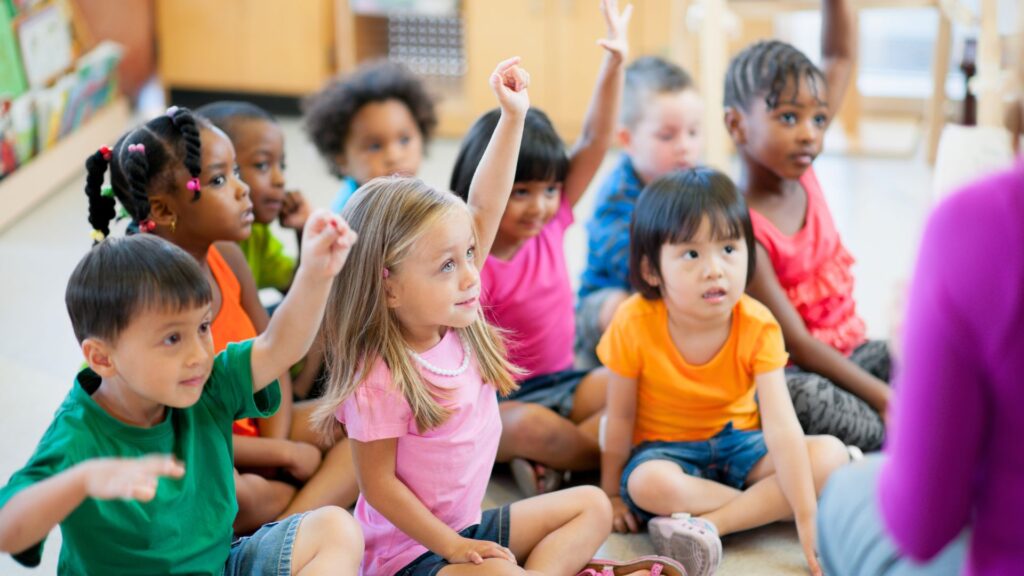 children in childcare sitting raising hands