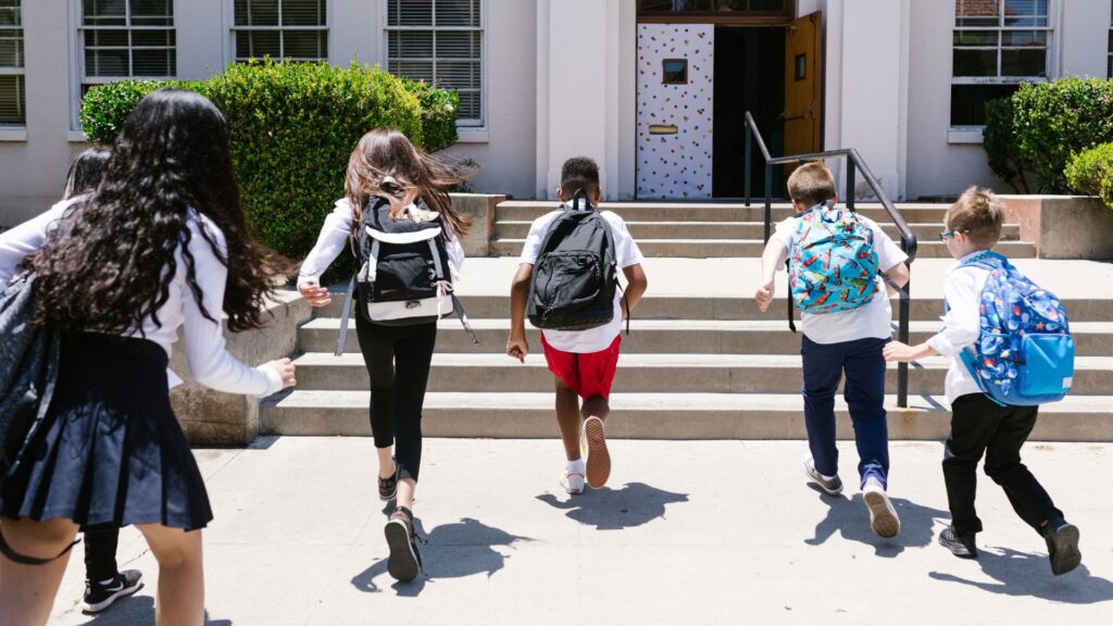 kids wearing school uniforms and backpacks run towards school steps