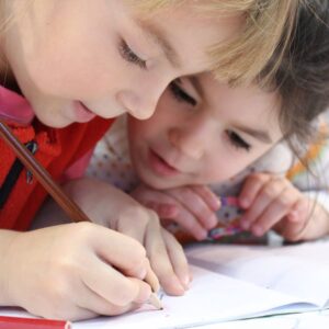 2 kids lean in together to drawing on paper 