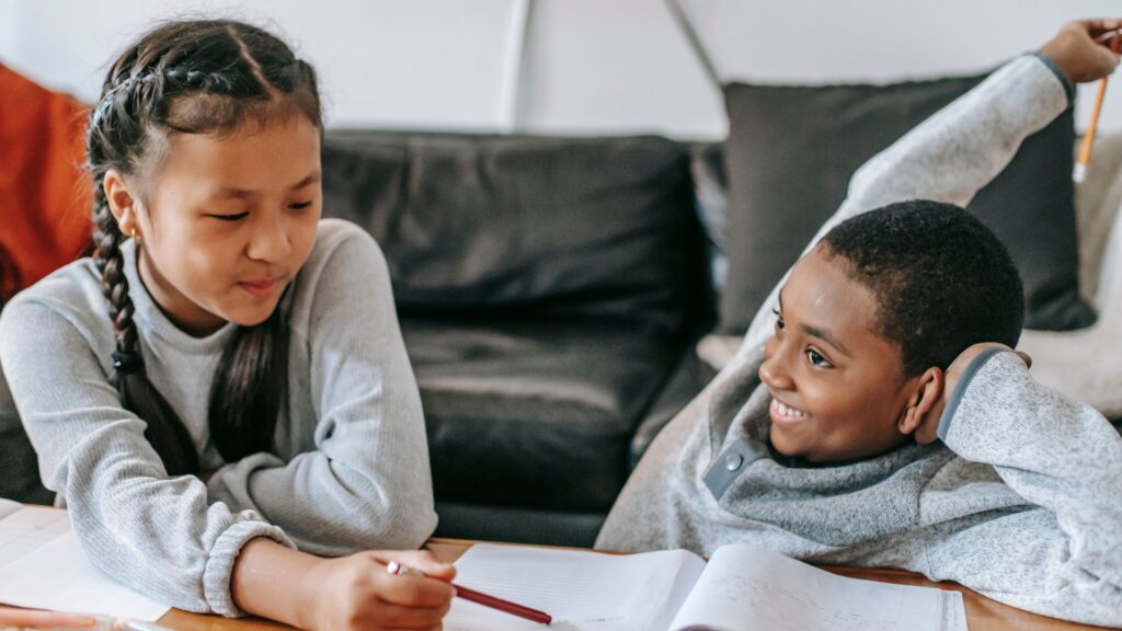 kids sit on floor smiling while looking at papers on table