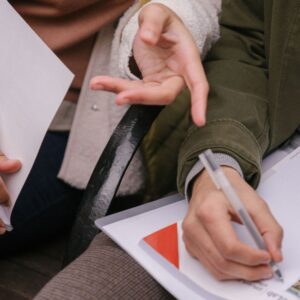 close up of person writing with someone else's hand pointing 